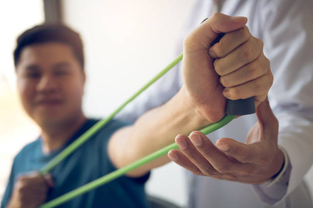 Close up hand patient doing stretching exercise with a flexible exercise band and a physical therapist hand to help in clinic room. stock photo