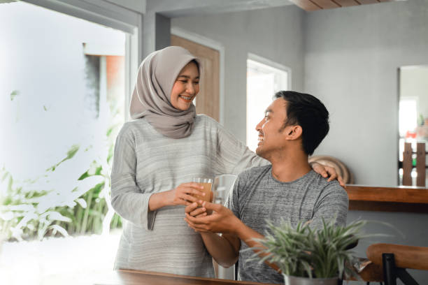 muslim woman served her husband with fruit juice beautiful asian muslim woman giving  a glass of juice to her husband at home malay couple stock pictures, royalty-free photos & images