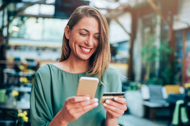 Girl holding credit card and texting Young woman sitting in a cafe and holding credit card and smart phone shopping photos stock pictures, royalty-free photos & images