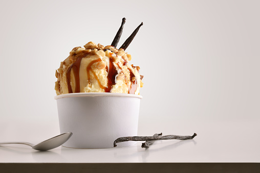 Composition of vanilla ice cream ball in paper cup on white table with products of ornament and elaboration isolated background. Horizontal composition. Front view.