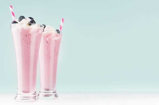 dwa koktajle z mleka jagodowego w eleganckim szkle ze słomkami, jagodami, bitą śmietaną w miękkim jasnoziemowym zielonym wnętrzu, kopiuj przestrzeń. - blueberry smoothie glass striped zdjęcia i obrazy z banku zdjęć