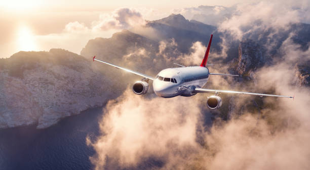 istock Airplane is flying over mountains and low clouds at sunset in summer. Landscape with passenger airplane, sky in clouds, rocks, sea, sunlight. Business travel. Commercial plane. Aerial view of aircraft 1148158341