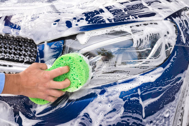 Man washing a soapy blue car with a green sponge.