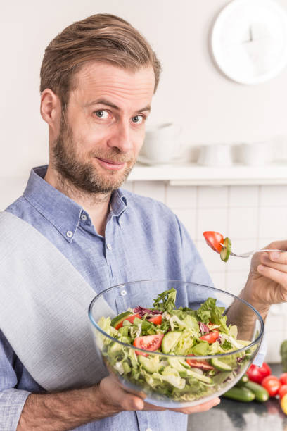 istock Happy smiling man eating fresh vegetable salad in the kitchen 1148161873