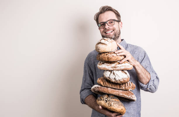 Happy baker man holding pile of rustic crusty breads