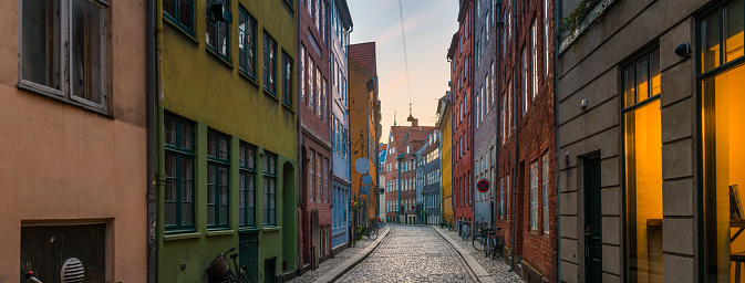 Colourful historic townhouses overlooking a quaint winding cobbled street at sunrise in the heart of Copenhagen, Denmark’s vibrant capital city.