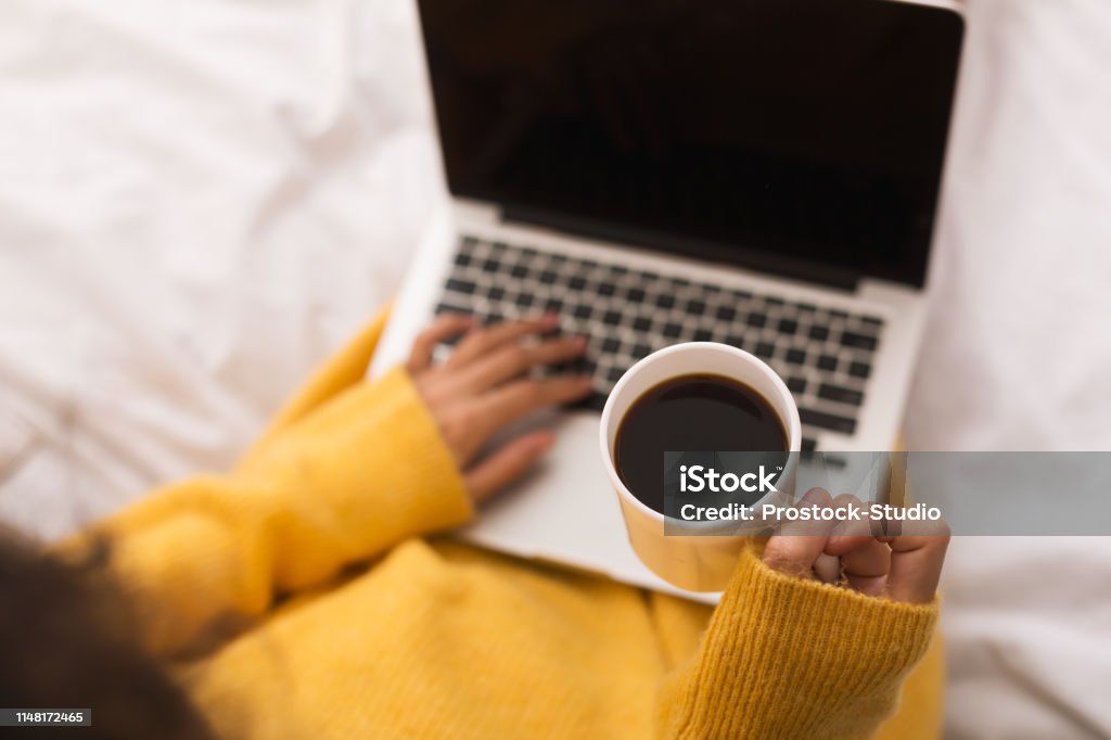 Woman surfing internet on laptop and drinking coffee Woman surfing internet on laptop and drinking coffee in bed Coffee - Drink Stock Photo