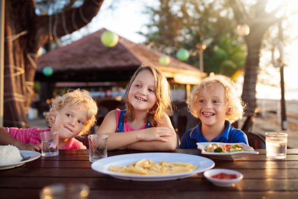 Family eating lunch on tropical beach. Kids in outdoor restaurant of exotic resort in Asia. Asian food for children. Little boy and girl eat dinner at sea coast. Holiday with child.