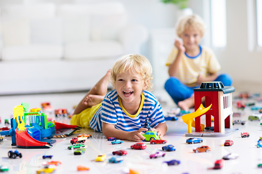 Kids play with toy cars in white room. Little boy playing with car and truck toys. Vehicle and transportation game for children. Kid with parking garage. Child having fun at home or daycare.