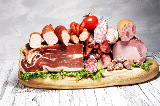 cold meat assortment with delicious salami and herbs . Variety of meat products including proscuitto, jamon  and sausages on wood