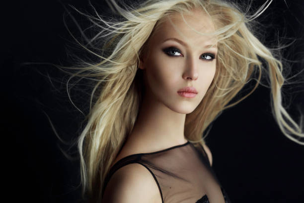 Graceful blonde girl in perfect make up with hair scattered by the wind, isolated on a black background. stock photo