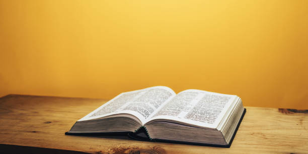istock Bible on a brown wooden table. Beutiful orange wall background. 1148178574