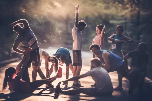 Marathon runners stretching and warming up before the race at sunset.