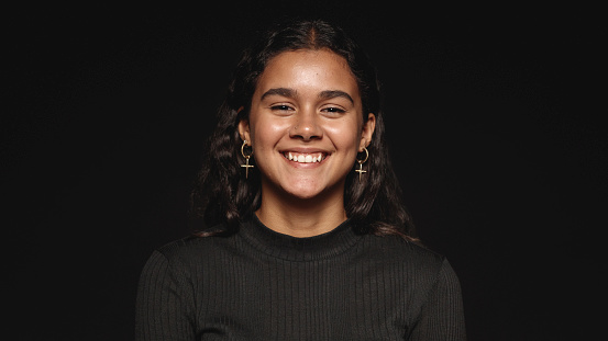 Close up of a smiling woman against black background. Young woman with a cute smile looking at camera.