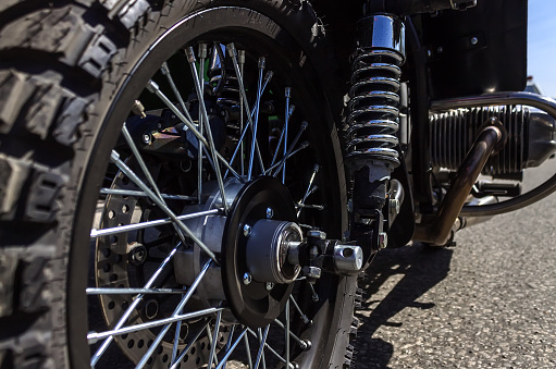 The front wheel of the motorcycle with spokes and reinforcement spring. Cylinder engine in the background