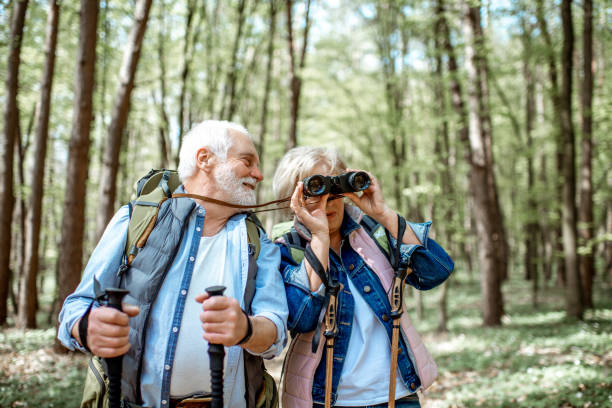 Senior couple hiking in the forest Beautiful senior couple hiking with backpacks and trekking sticks in the forest. Concept of active lifestyle on retirement bird watching stock pictures, royalty-free photos & images