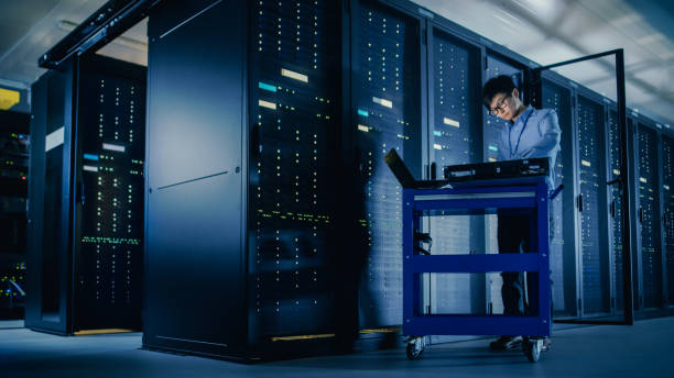 istock In Data Center: Male IT Technician Running Maintenance Programme on a Laptop, Controls Operational Server Rack Optimal Functioning. Modern High-Tech Telecommunications Operational Super Computer. 1148195858