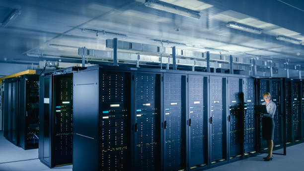 istock In Data Center: Female IT Technician Stands before Open Server Rack Cabinet, Uses Laptop Computer to Run Maintenance Diagnostics so that Mainframe Works at Optimal Functioning Level. 1148195899