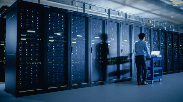 istock In the Modern Data Center: IT Engineer Doing Maintenance and Diagnostics. Pushes Cart alongside Server Racks. Planned System Equipment Update and Maintanence. 1148195930