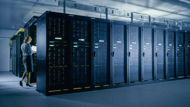 istock In Data Center: Female IT Technician Walks Between Rows of Server Racks, Uses Laptop Computer to Run Maintenance Diagnostics so that Mainframe Works at Optimal Functioning Level. 1148195994