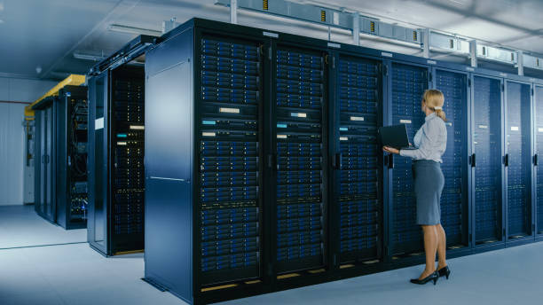istock In Data Center: Female IT Technician Stands Near Rack Cabinet and Runs Maintenance Program on Laptop, Controls Operational Server's Optimal Functioning. 1148196023