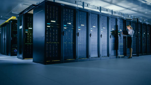 istock In Data Center: Female IT Technician Stands before Open Server Rack Cabinet, Uses Laptop Computer to Run Maintenance Diagnostics so that Mainframe Works at Optimal Functioning Level. 1148196135