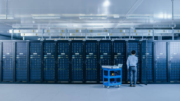 istock In the Data Center: IT Engineer Working with Server Racks Works with Opened Cabinet to Installs New Hardware for System Update, Cart Stands Beside the Row of Server Racks. Engineer Doing Maintenance. 1148196171