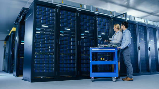 istock In the Modern Data Center: Engineer and IT Specialist Work with Server Racks, on a Pushcart Equipment for Installing New Hardware. Specialists Doing Maintenance of the Database. Low Angle Shot. 1148196257