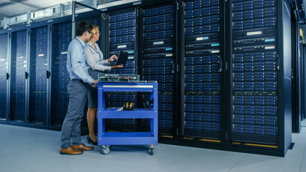 istock In the Modern Data Center: Engineer and IT Specialist Work with Server Racks, on a Pushcart Equipment for Installing New Hardware. Specialists Doing Maintenance and Diagnostics of the Database. 1148196374