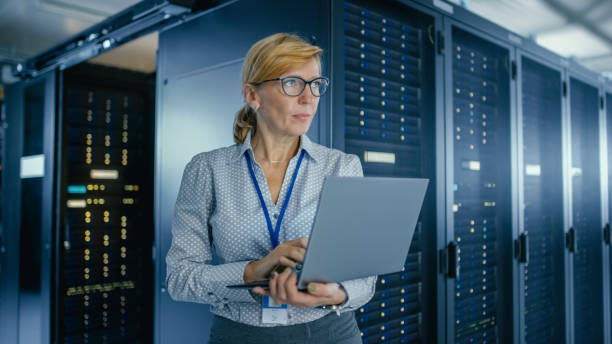 in data center: female it technician running maintenance programme on a laptop, controls operational server rack optimal functioning. modern high-tech telecommunications operational data center. - network server rack computer mainframe imagens e fotografias de stock