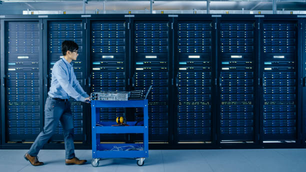 istock In the Modern Data Center: IT Engineer Pushes Cart alongside Server Racks and Cabinets to Install New Hardware for Planned System Update, Equipment Replacement. 1148196933