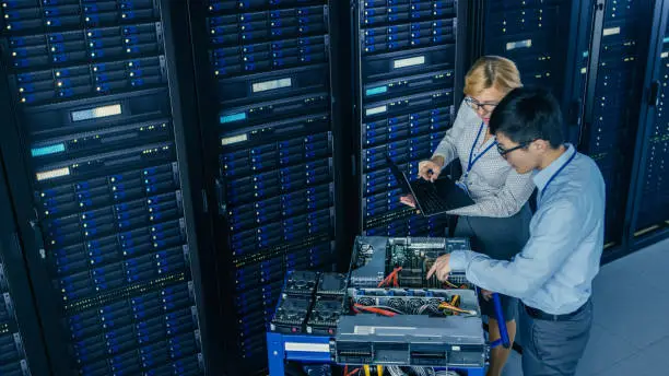 Photo of In the Modern Data Center: Engineer and IT Specialist Work with Server Racks, on a Pushcart Equipment for Installing New Hardware. Specialists Doing Maintenance and Diagnostics of the Database.