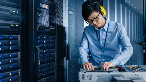 istock In Data Center: IT Engineer Wearing Protective Muffs Installs New Hardware for Server Rack. Specialist Doing Maintenance, Running Diagnostics and Updating Hardware for Stable Functioning of a System. 1148197018