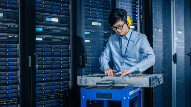 istock In the Modern Data Center: IT Engineer Wearing Protective Muffs Installs New Hardware for Server Rack. IT Specialist Doing Maintenance, Updating Hardware for Stable Functioning of Database System. 1148197040