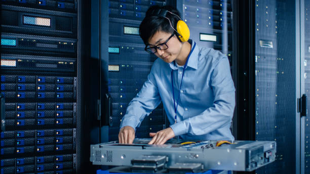istock In the Modern Data Center: IT Engineer Wearing Protective Muffs Installs New Hardware for Server Rack. IT Specialist Doing Maintenance, Updating Hardware for Stable Functioning of Database System. 1148197191