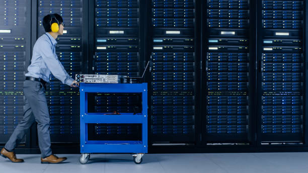 In the Modern Data Center: IT Engineer Doing Maintenance and Diagnostics. Pushes Cart alongside Server Racks, Opens Cabinet to Install New Hardware for Planned System Update, Equipment Replacement.