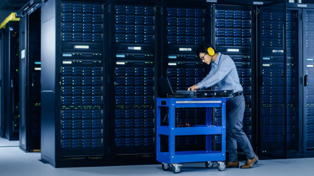 istock In Data Center: IT Engineer Wearing Protective Muffs Installs New Hardware for Server Rack. Specialist Doing Maintenance, Running Diagnostics and Updating Hardware for Stable Functioning of a System. 1148197256