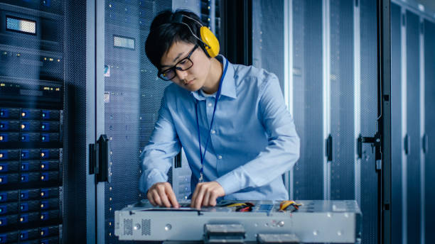 istock In the Modern Data Center: IT Engineer Wearing Protective Muffs Installs New Hardware for Server Rack. IT Specialist Doing Maintenance, Running Diagnostics for Stable Functioning of Database System. 1148197278
