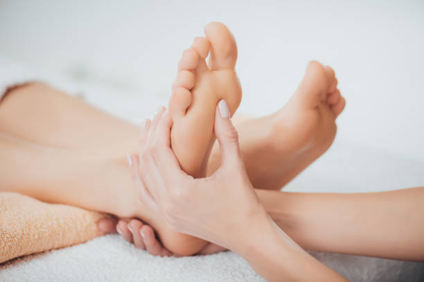 cropped view of masseur doing foot massage to adult woman in spa stock photo