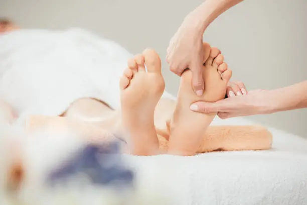 selective focus of masseur doing foot massage to adult woman in spa