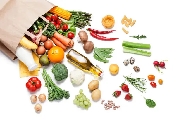 Top view of a paper bag full of different food shot on white background. The paper bag is laying on the white background and the food is coming out from it. Food included in the composition are vegetables, fruits, dairy products, meat, pasta, eggs, cooking oil and others. DSRL studio photo taken with Canon EOS 5D Mk II and Canon EF 70-200mm f/2.8L IS II USM Telephoto Zoom Lens