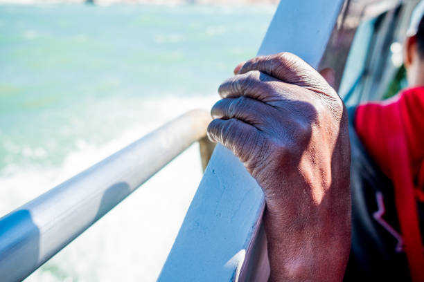 close up of thin and skinny african migrant man hand on boat while crossing mediterranean sea to europe on sunny day as symbol of refugees crisis stock photo