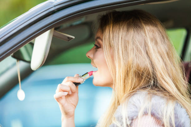 istock Young woman applying lipstick in car 1148206757