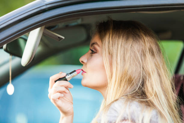 istock Young woman applying lipstick in car 1148207163