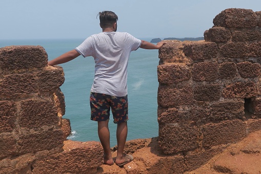 Indian man standing looking out to sea in Cabo De Rama Fort ruins, Goa, India