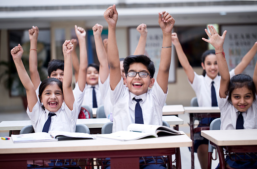 Group of excited school children cheering in classroom
