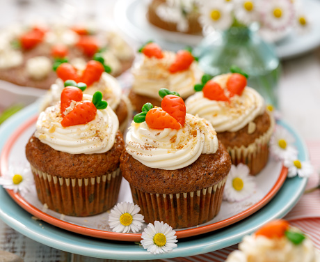 Carrot cake muffins with mascarpone cream,  topped with marzipan carrots on a plate. Delicious homemade dessert.