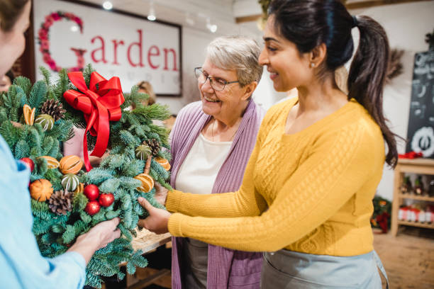 Choosing a Christmas Wreath at the Florist Women are admiring a Christmas wreath in a florist shop. small business saturday stock pictures, royalty-free photos & images