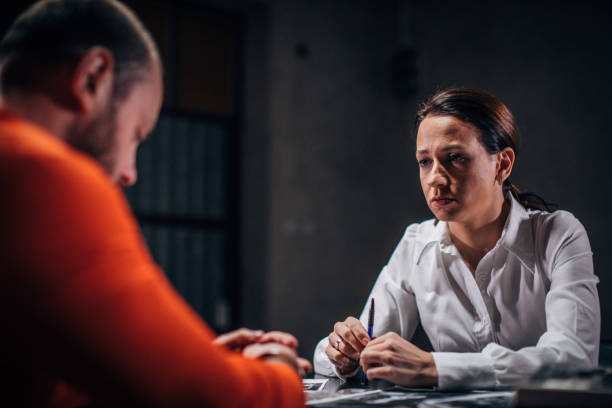 Prisoner and female detective Prisoner in orange jumpsuit with handcuffs and female detective sitting in the investigation room police station stock pictures, royalty-free photos & images