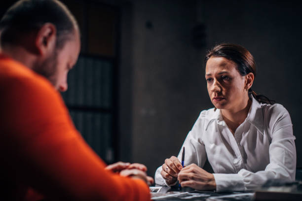 Prisoner and female detective Prisoner in orange jumpsuit with handcuffs and female detective sitting in the investigation room killercell stock pictures, royalty-free photos & images